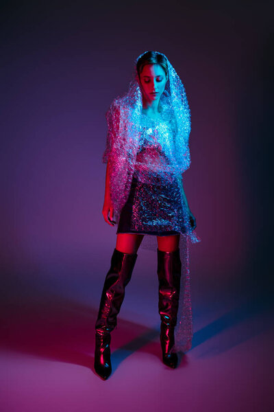 A woman stands enveloped in bubble wrap, her pose delicate and calm under the colorful lights.