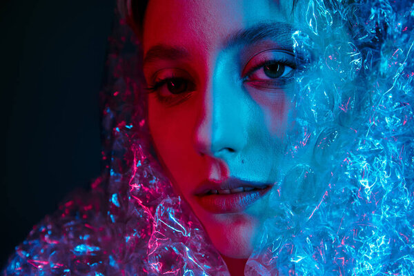 Woman's face glows under neon lights, half hidden by translucent material