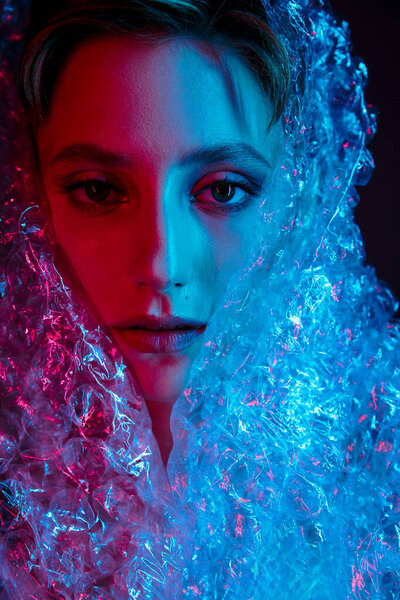 A woman's face is illuminated by pink and blue light, obscured by a translucent, bubble-like fabric.