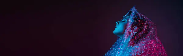 stock image A woman's face glows under a vibrant blue and pink light, covered in a bubble wrap-like material.