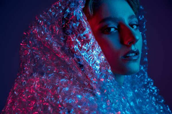 A woman's face is illuminated by red and blue light, partially obscured by a sheet of bubble wrap.