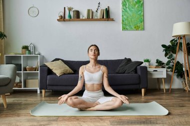 Genç bir kadın modern dairesinde yoga yapıyor, meditasyon yoluyla huzur ve farkındalık buluyor..