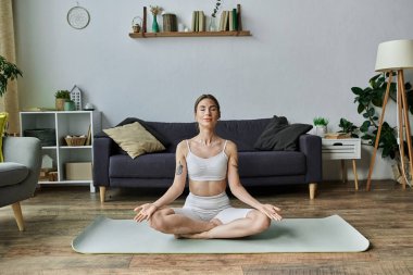 Vitiligo 'su olan genç bir kadın modern oturma odasındaki paspasın üzerinde otururken yoga pozunda meditasyon yapıyor..