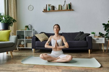 Vitiligo 'su olan genç bir kadın modern bir dairede meditasyon yapıyor, yoga pozunda mindere oturuyor..