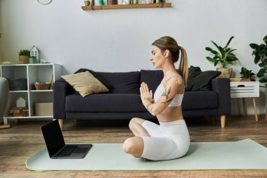 Beyaz etek giyen genç bir kadın modern bir dairede yoga minderinde oturur ve gözleri kapalı meditasyon yapar..