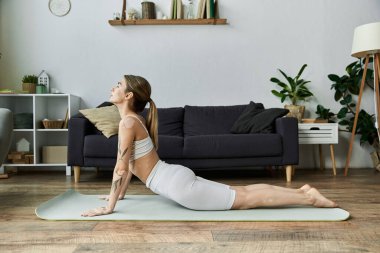 Aktif giyimli genç bir kadın modern bir dairede yoga yapıyor..