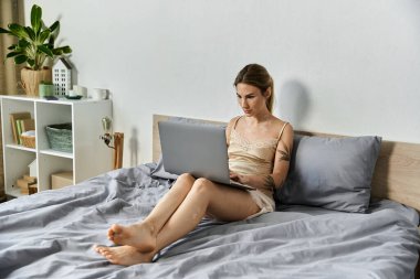 İpek bluzlu genç bir kadın yatağında dizüstü bilgisayar kullanıyor..