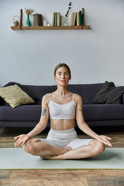 Молодая женщина с витилиго практикует йогу в современной квартире, находя мир и внутреннюю силу через внимательную медитацию.