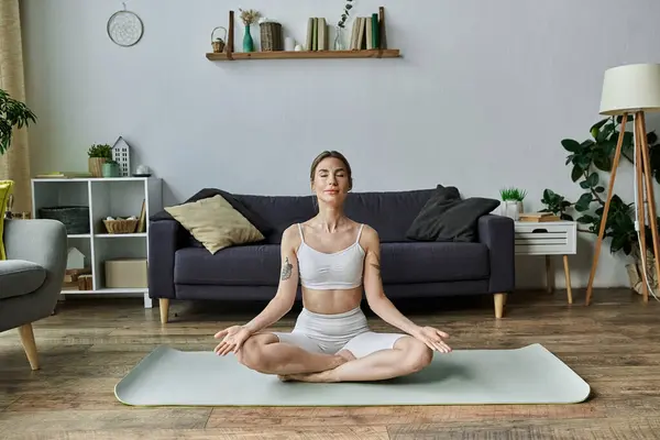 stock image A young woman with vitiligo meditates in a comfortable yoga pose while sitting on a mat in her modern living room.