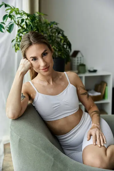 stock image A young woman in activewear sits on a chair in a modern apartment, practicing yoga.