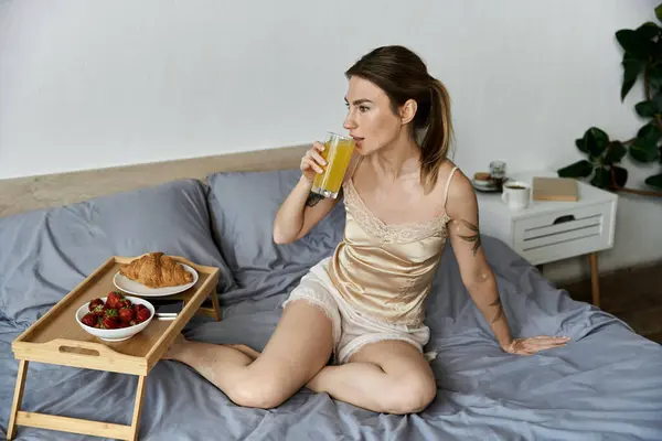 stock image A young woman in a silk top enjoys a breakfast of fruit and pastries in her bed.