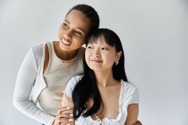 İki genç kadın, basit bir beyaz arka plana karşı hassas bir anı paylaşıyor..