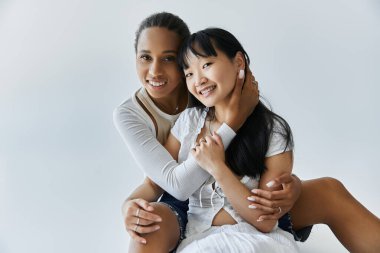 Irklar arası lezbiyen bir çift, basit bir gri arka plana karşı birbirlerini kucakladıkları hassas bir anı paylaşıyor..