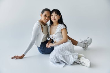 İki genç kadın, lgbtq çifti, şefkat dolu gözlerle gülümseyen beyaz bir arka plana nazikçe sarılıyorlar.