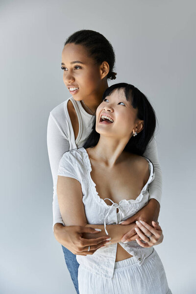 Две молодые женщины обнимают друг друга с любовью на нейтральном сером фоне..