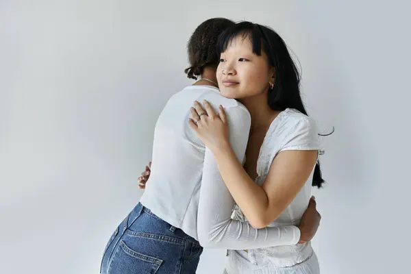 stock image A young African American woman embraces her Asian partner against a grey backdrop.