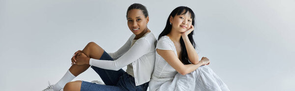 Две молодые женщины, лесбийская пара, сидят спина к спине в студии, наслаждаясь нежным моментом вместе.