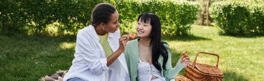 İki genç kadın, yemyeşil çimlerle çevrili açık havada piknik yapıyor..