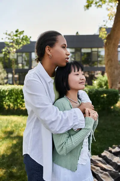 stock image A young African American woman lovingly embraces her Asian partner while outdoors.