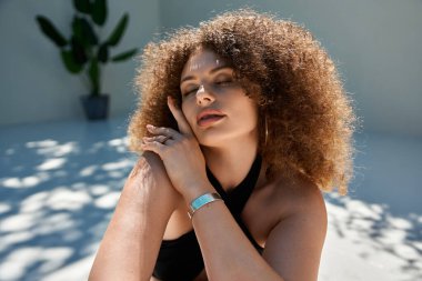 Kıvırcık saçlı güzel bir kadın siyah bir mayo giyer ve yaz güneşinin tadını çıkarır..