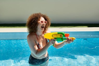 Bikinili bir kadın havuza su tabancası fırlatırken gülüyor..
