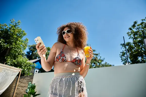 stock image A woman in a bikini enjoys a summer day by the pool, sipping juice and checking her phone.