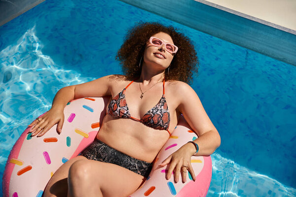 A woman in a bikini relaxes on a donut float in a pool.