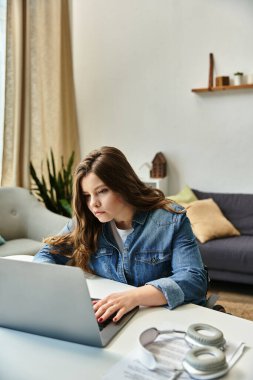 Tekerlekli sandalyedeki genç bir kadın, parlak ve modern bir dairede laptopuyla çalışıyor..