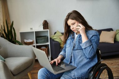 Tekerlekli sandalyedeki genç bir kadın telefondayken dizüstü bilgisayar kullanıyor. Modern dairesinde rahatça konuşabiliyor..