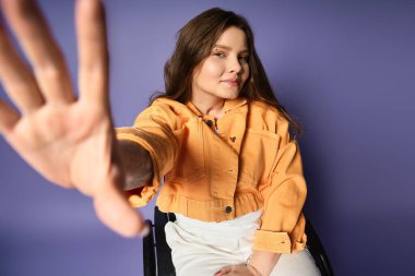 A young woman in a yellow jacket with long brown hair reaches out with one hand while sitting in a wheelchair clipart