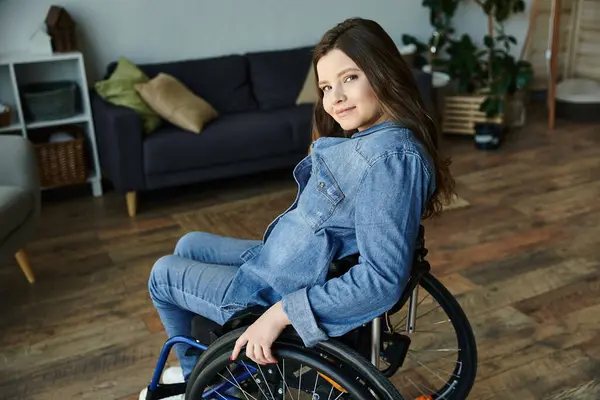 Stock image A young woman smiles while sitting in her wheelchair in a modern apartment, showcasing a comfortable and accessible lifestyle.