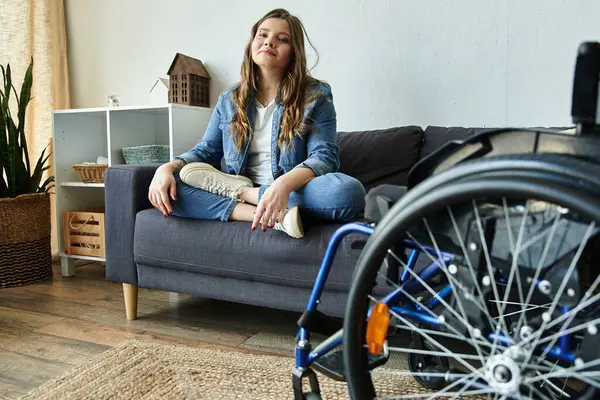 stock image A young woman sits comfortably on a couch in a modern apartment, her wheelchair nearby.