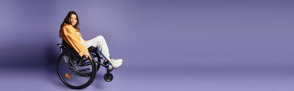 Молодая женщина в модной повседневной одежде сидит в инвалидном кресле на фиолетовом фоне.