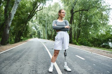 A young woman in sportswear embraces the outdoors as she works out confidently with her prosthetic leg. clipart