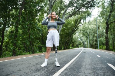 A young woman with a prosthetic leg embraces fitness while enjoying nature along a picturesque route. clipart