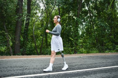 Spor kıyafetleri içinde genç bir kadın ağaçlık bir yolda koşuyor. Formu ve doğayı kararlılıkla kucaklıyor..