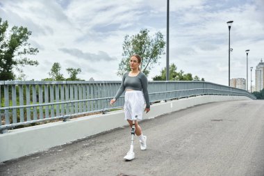 A young woman in sportswear confidently walks along a bridge, embracing her active lifestyle outdoors. clipart