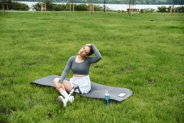 Protez bacaklı genç bir kadın güneşli bir günün tadını çıkarıyor. Spor kıyafetleriyle çimlerin üzerinde egzersiz yapıyor..