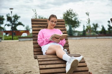 Genç bir kadın dışarıda kitap okuyor, protez bacağını gösteriyor.