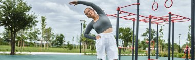 Spor kıyafetleri içinde genç bir kadın açık havada mutlu bir şekilde uzanıyor, canlı bir parkta spor ve hareketten zevk alıyor..