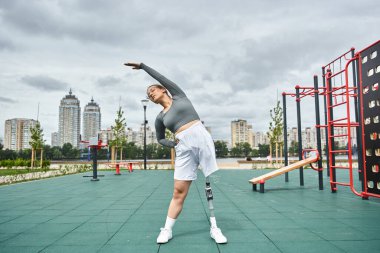 Protez bacaklı genç bir kadın canlı bir şehir parkında spor yaparken zarifçe esniyor..