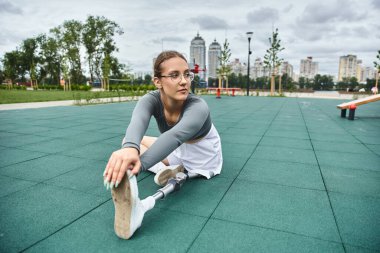 Kararlı genç bir kadın, şık spor kıyafetlerinde zindelik ve esnekliği kucaklayarak bacaklarını dışarı uzatıyor..