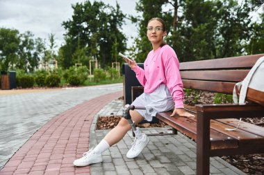 A determined young woman with a prosthetic leg using smartphone clipart