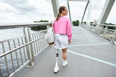 A young woman in sportswear enjoys a day outdoors while confidently walking a bridge. clipart