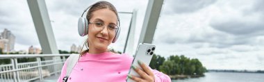 A young woman smiling and holding smartphone, listening music in headphones clipart