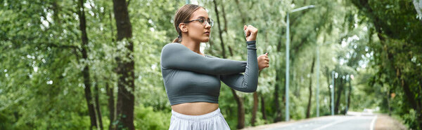 Молодая женщина в спортивной одежде простирается на открытом воздухе, охватывая фитнес и природу