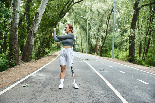 A young woman with a prosthetic leg exercises outdoors, embracing a healthy lifestyle surrounded by trees.