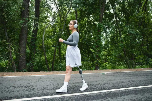 Spor kıyafetleri içinde genç bir kadın ağaçlık bir yolda koşuyor. Formu ve doğayı kararlılıkla kucaklıyor..