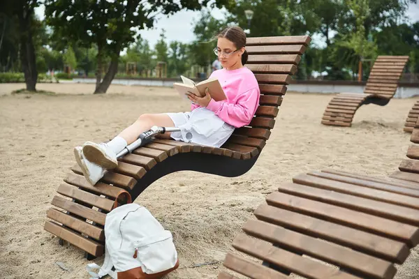 stock image A young woman relaxes on unique seating, immersed in a book, showcasing resilience and joy in nature.