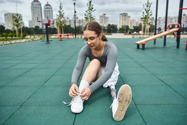 stock image A determined young woman ties her shoe while engaged in an outdoor fitness session.